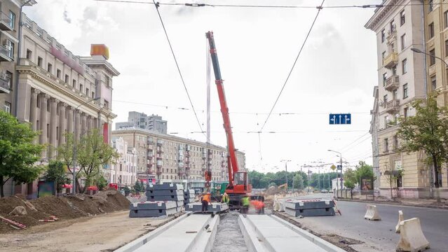Installing concrete plates by crane at road construction site panoramic timelapse. Industrial workers with hardhats and uniform. Reconstruction of tram tracks in the city street