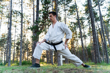 Naklejka na ściany i meble A young man doing karate in the forest training strength pose meditation 