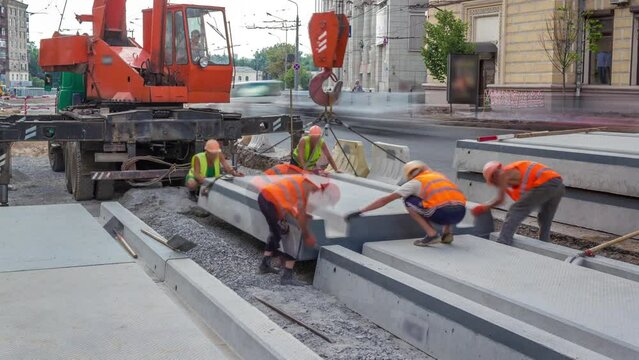 Installing concrete plates by crane at road construction site timelapse. Industrial workers with hardhats and uniform. Reconstruction of tram tracks in the city street