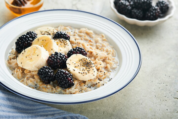 Oatmeal. Bowl of oatmeal porridge with blackberry, bananas and chia seeds on gray concrete old table background. Top view in flat lay style. Natural ingredients Hot and healthy breakfast and diet food