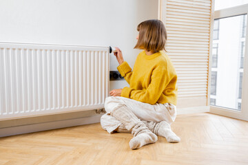 Woman controls room temperature with a thermostat on radiator, feeling cold at home. Concept of...