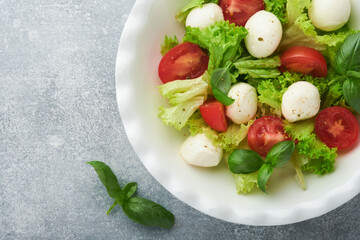 Caprese salad. Italian caprese salad with sliced tomatoes, mozzarella cheese, basil, olive oil in white plate over white background. Delicious Italian food. Top view. Rustic style.