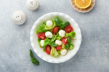 Caprese salad. Italian caprese salad with sliced tomatoes, mozzarella cheese, basil, olive oil in white plate over white background. Delicious Italian food. Top view. Rustic style.