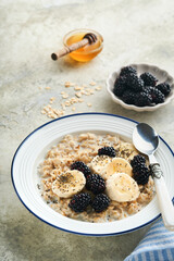 Oatmeal. Bowl of oatmeal porridge with blackberry, bananas and chia seeds on gray concrete old table background. Top view in flat lay style. Natural ingredients Hot and healthy breakfast and diet food