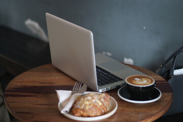 Croissant, coffee and laptop on the wood 