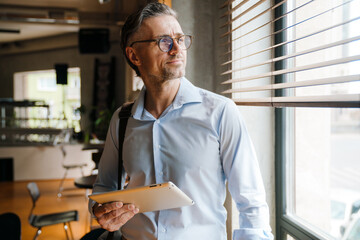 Naklejka na ściany i meble European grey man in eyeglasses using tablet computer in office