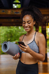 Young black woman smiling while using cellphone after practice