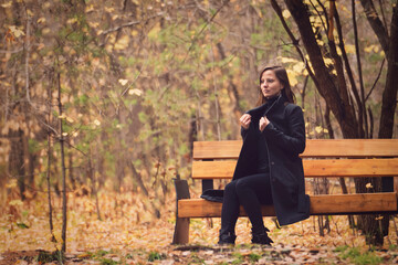 beautiful young woman on a park bench. Beautiful and cozy autumn, rustling foliage underfoot, lyrical autumn mood copy space