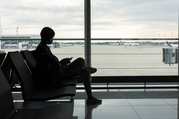 Silhouette shot of asian woman with face mask who is sitting on bench in the airport with relaxing...