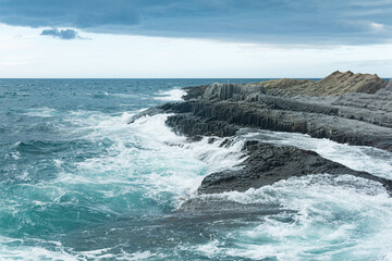 Fototapeta na wymiar rocky seashore formed by columnar basalt against the backdrop of a stormy sea, coastal landscape of the Kuril Islands