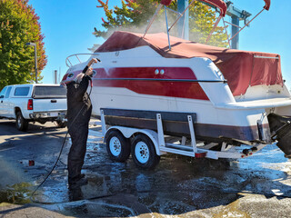 Man using a pressure washer to clean power boat on a trailer