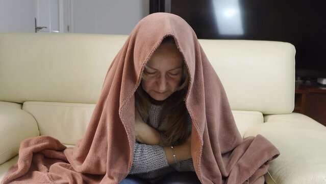 Woman covered with a blanket and going cold from the energy crisis and the high price of gas.