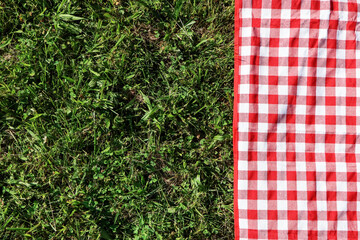 Checkered picnic tablecloth on fresh green grass, top view. Space for text