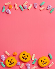 Halloween sweet background frame with scary pumpkin cookies, candy and Halloween decor on pink table