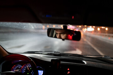 Look of man is reflected in rear-view mirror traveling in car in evening hurries home after work....