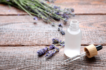 Obraz na płótnie Canvas Bottle of lavender essential oil with flowers on wooden table, space for text