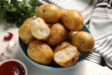 Bowl of tasty whole baked potatoes and sauce on white table, closeup