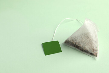 New tea bag with tab on light green background, closeup. Space for text