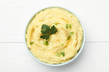 Bowl of tasty mashed potatoes with parsley and green onion on white wooden table, top view