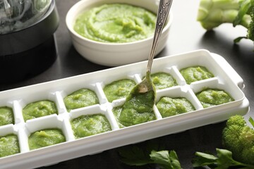 Putting puree with spoon into ice cube tray on table, closeup. Ready for freezing