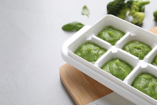 Broccoli puree in ice cube tray ready for freezing and ingredients on light table, closeup. Space for text