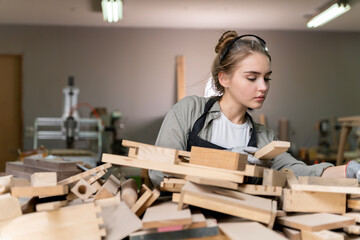 A beautiful woman carpenter is standing to choose a piece of wood to use in her creation.