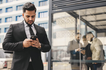 Portrait of a business man outdoors using the phone against the backdrop of a glass building downtown.
