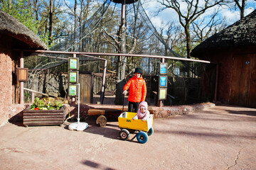 Boy pulls wooden trolley with sister at zoo.