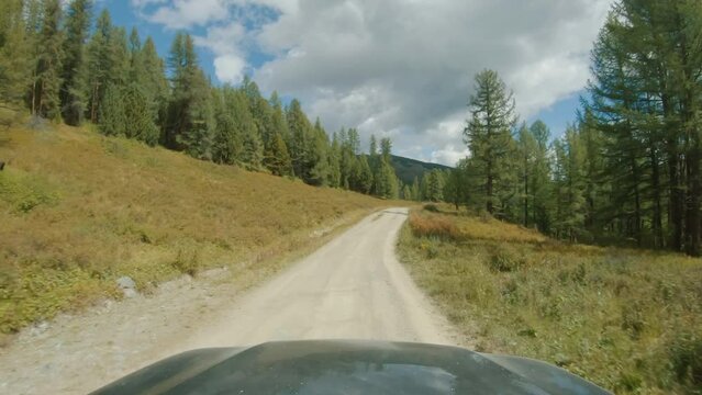Car driving on a gravel road past fields and trees. Car riding on country dirt road. Discovery and adventure travel concept. POV, onboard camera, sunny day