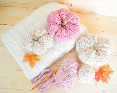 beige and soft pink crochet woolen pumpkin obn a white woolen blanket with woolen balls, crocjet hook and autumn leaves on wooden ground