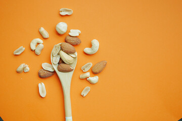 top view of many mixed nuts on wooden spoon on orange background 