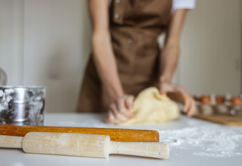A woman in a special apron cooks at home. Rolling out and preparing dough for baking.
