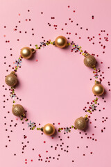 Obraz premium Circle frame of golden Christmas balls and glitter confetti stars on pink background