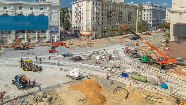 Road construction site with concrete works for road construction with many workers in uniform and many machines with trucks and bulldozers panoramic aerial timelapse. Reconstruction of tram tracks