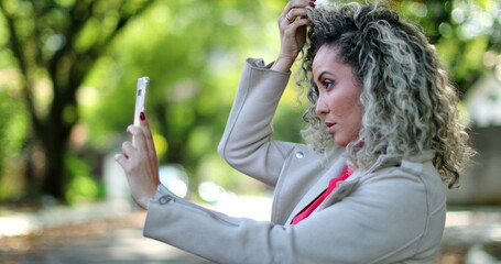 Woman adjusting hair and face in front of cellphone camera outside