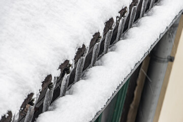 Obraz premium The water freeze on the roof when flows to the spout. Frozen outflow of water from the roof of the house. Icicles on a snowy roof.