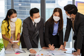 Asian corporate team wearing medical face mask brainstorming, discussing and sharing idea of new project at office. new normal working and social distancing during Coronavirus epidemic concept