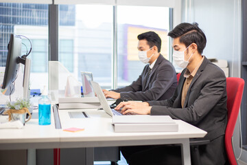 Group of Asian employees wearing medical mask working on computer at desk in the office