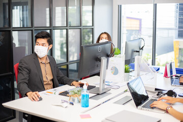 Asian employees wearing medical mask working on computer at desk in the office