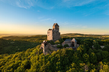 Renewed historical monument in Hungary Mountains. Aerial landscape photo about a medieval castle ruins near by Holloko town. Panoramic landscape photo with forest and amazing sunset