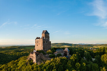 Renewed historical monument in Hungary Mountains. Aerial landscape photo about a medieval castle ruins near by Holloko town. Panoramic landscape photo with forest and amazing sunset
