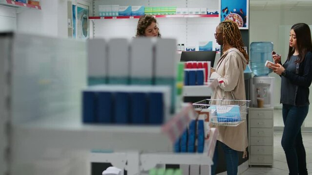 Multiethnic group of people buying pills and supplements from drugstore desk using smartwatch, credit card or mobile phone with nfc. Paying at pharmacy counter for medicaments.