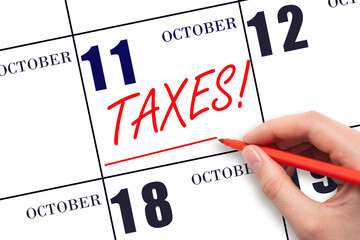 Hand drawing red line and writing the text Taxes on calendar date October 11. Remind date of tax payment