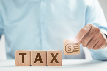 TAX on wooden cubes. Businessman's hand holding a wooden block with coin or money icon and a wooden block with the word TAX. Business and finance concept. Taxes and taxation. The tax burden.
