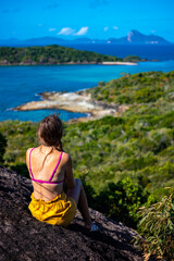 A beautiful girl sits on top of a mountain overlooking a panorama of the whitsunday islands; relaxing on paradise beaches in the whitsunday islands, queensland, australi