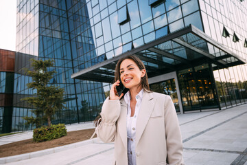 Young cheerful business woman working with a mobile phone in the street with office buildings in the background