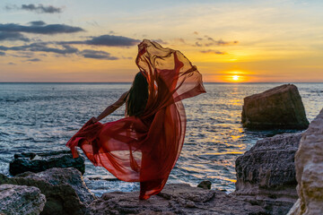 a dancing woman in a red flying dress on the ocean or on the sea beach against the backdrop of the...