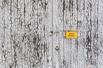 Abgeplatzer weißer Lack an einer Holzwand mit einem Schild "Ausfahrt freihalten"