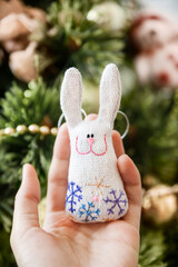 Woman holds cute handmade rabbit with embroidered snowflakes. DIY decoration for Christmas tree....