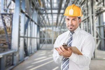 Professional young man with a clipboard posing on construction site.